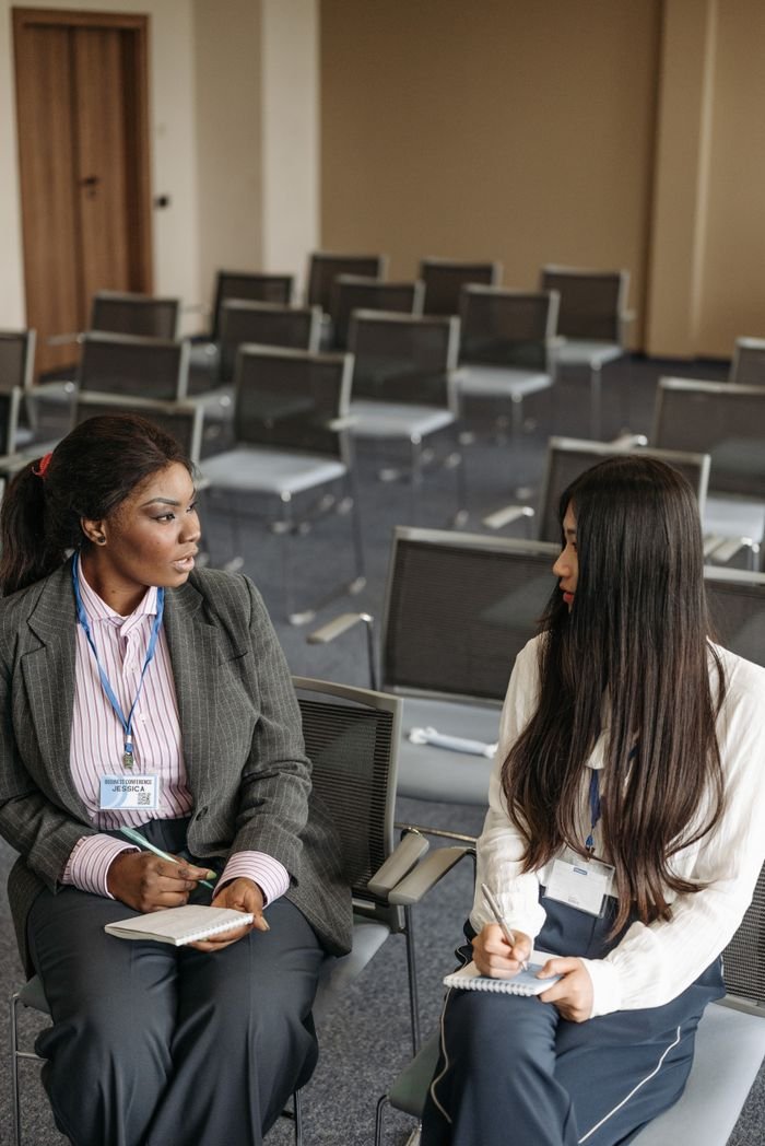 Services Two women engage in a discussion during a conference in a meeting room.